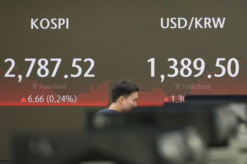 A currency trader walks by the screen showing the Korea Composite Stock Price Index (KOSPI), left, and the foreign exchange rate between U.S. dollar and South Korean won at a foreign exchange dealing room in Seoul, South Korea, Wednesday, July 3, 2024. Asian shares were mostly higher on Wednesday after Tesla gained more than 10%, helping to drive U.S. benchmarks to more records. (AP Photo/Lee Jin-man)