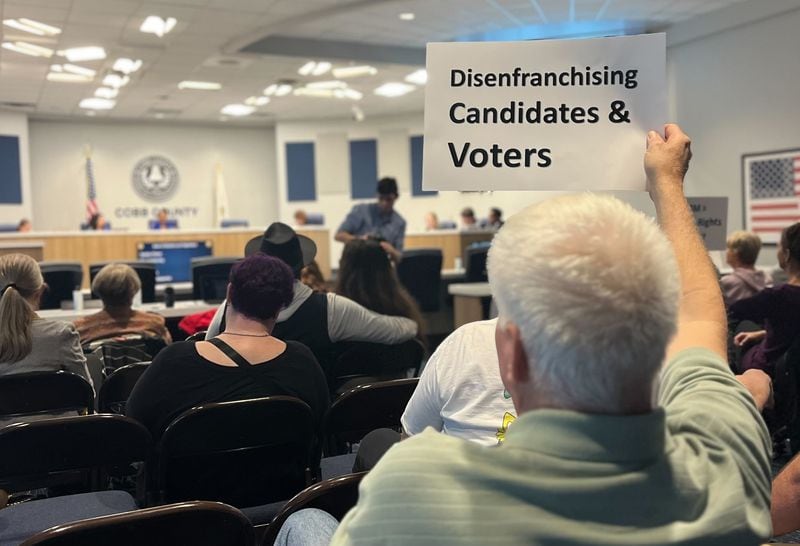 A resident holds a sign in protest at a Cobb County Board of Elections and Registration meeting in March.