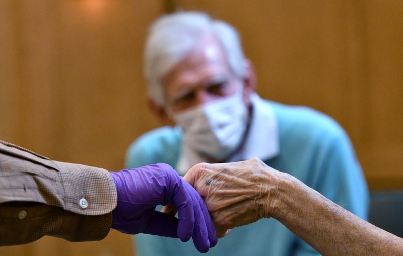 William Kendrick holds a hand of his mother, Connie Kendrick, as he and Sam Allen (background), Connie's brother, visit her face-to-face after months of visitation restrictions at The William Breman Jewish Home in Atlanta. (Hyosub Shin / Hyosub.Shin@ajc.com)