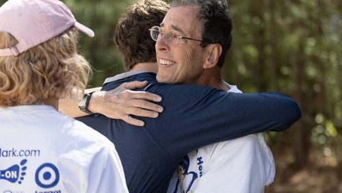 Clark Howard gets a hug from his son Grant Howard before the start of the Atlanta Habitat for Humanity dedication of the 98, 99, and 100th Howard's sponsored homes in Atlanta on Saturday, April 13, 2024.  (Steve Schaefer/steve.schaefer@ajc.com)