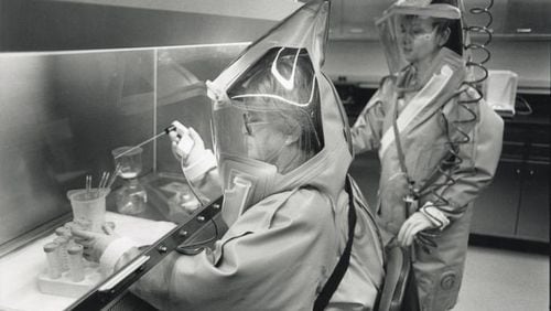 The Centers for Disease Control, founded here in 1946 as the Communicable Disease Center, originally focused on malaria control but now handles a wide range of public health issues. In this 1988 photo, Bertha Farrah, left, and Gilda Perez, medical technologists at the CDC virology lab, work in the maximum containment lab for the most dangerous viruses. The pair work wearing 15-pound laminated plastic suits connected to oxygen lines. RICH ADDICKS / AJC FILE