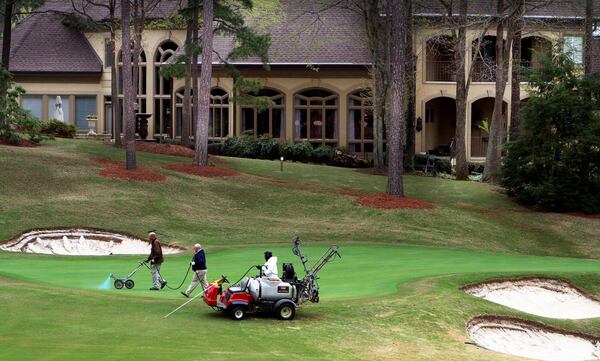 Grounds crews work on a green as a huge home sits nearby on the golf course at the Country Club of the South in Johns Creek. (AJC File)