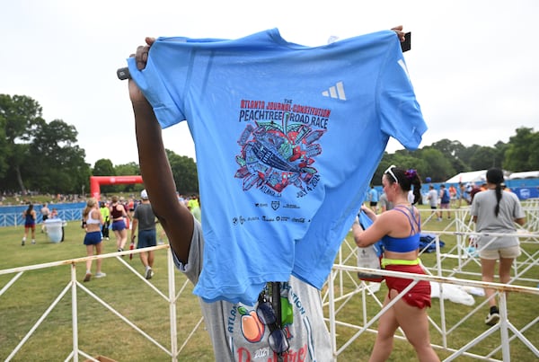 A volunteer shows off 2024 AJC Peachtree Road Race T-shirt at Piedmont Park during the 55th running of The Atlanta Journal-Constitution Peachtree Road, Thursday, July 4, 2024, in Atlanta. (Hyosub Shin/AJC)